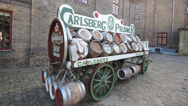 A sign reading Carlsberg Pilsner sits above a beer wagon filled with wooden kegs