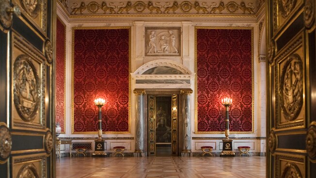 A palace room decorated in Rococo ornaments and velvet wallpaper with double doors opening to another room