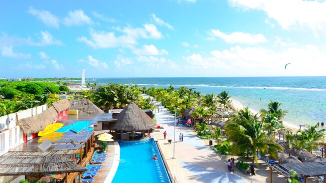 A beach club with a pool, outdoor recliners and a theme of thatched roofs evident in its buildings