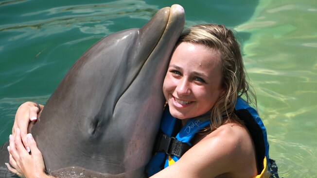 A girl hugs a dolphin and touches faces with the animal