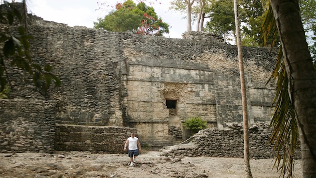 A man walking by the Kohunlich Mayan Ruins in an outdoor area featuring trees A man walking by the Kohunlich Mayan Ruins in an outdoor area featuring trees