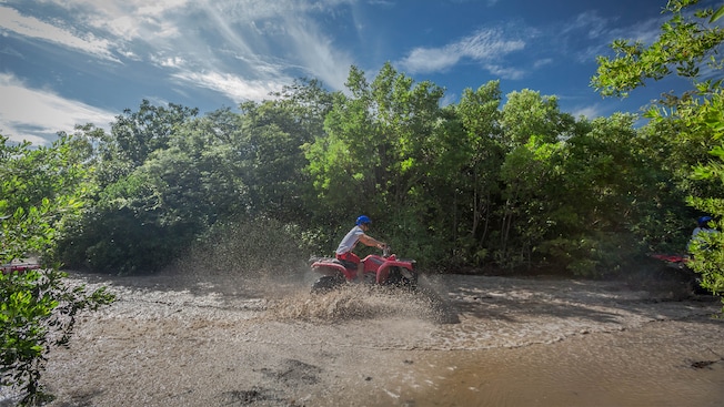 A man drives his ATV through a huge mud puddle in a forest