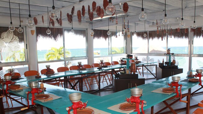 A room featuring long tables with chocolate workshop tools, chairs and windows overlooking the ocean