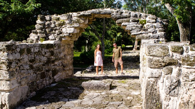 Una pareja se detiene a observar una estructura de piedra de aspecto antiguo con un arco