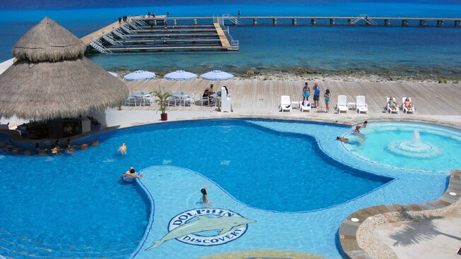 Lounge chairs occupy a wooden strip between a large shallow pool and a closed in ocean lagoon