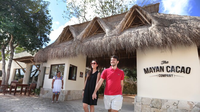 Una pareja camina hacia la entrada de techo de paja de la Mayan Cacao Company