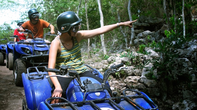 A girl on a stopped ATV smiles as she points to something within the forest A girl on a stopped ATV smiles as she points to something within the forest