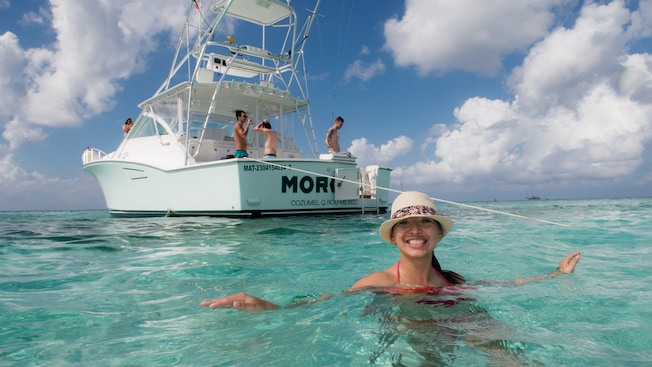 4 people stand on a boat while a woman smiles in the water 4 people stand on a boat while a woman smiles in the water