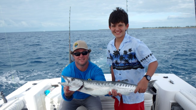 Padre e hijo posan con un gran pescado en un bote Padre e hijo posan con un gran pescado en un bote