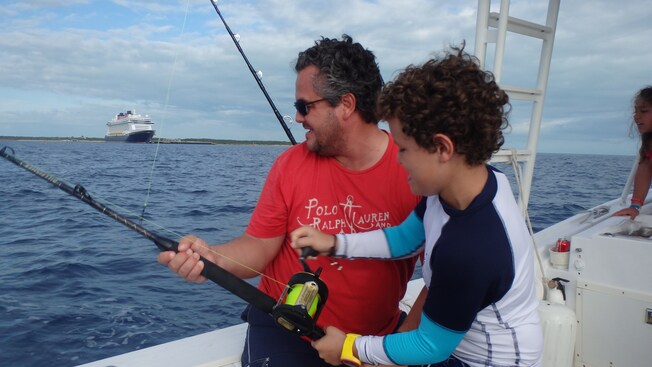 A man holds a fishing reel while a young boy reels in the catch