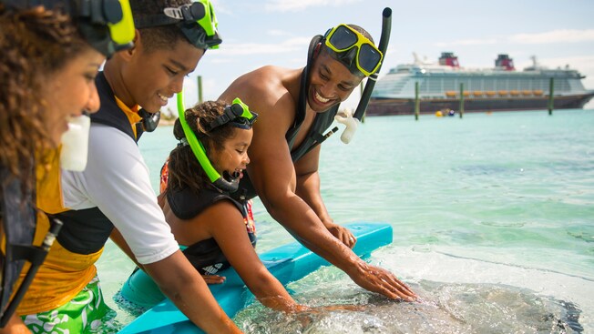 A young family gathers around a stingray to pet and interact with the animal