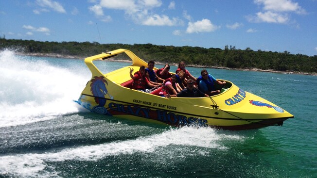 A group of people on a speed boat with a sign that reads Crazy Horse Jet Boat Tours