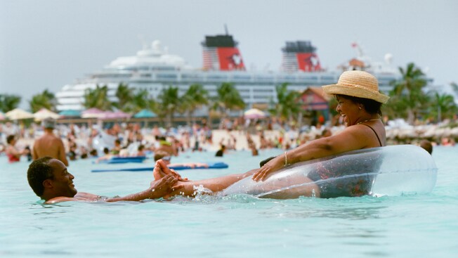 A man smiles as he tugs on the feet of a woman laughing in an inflatable tube