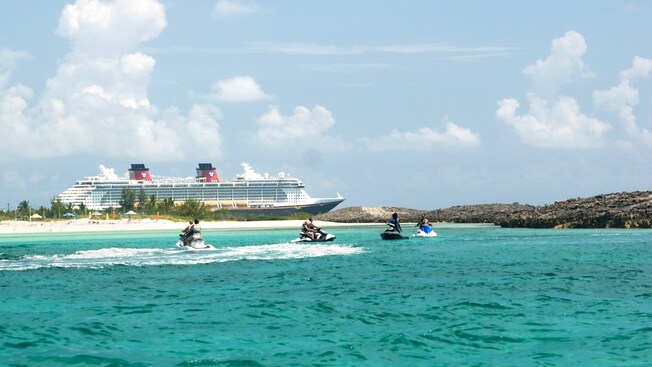 A group of Guests race across the ocean on water scooters in front of a Disney cruise ship