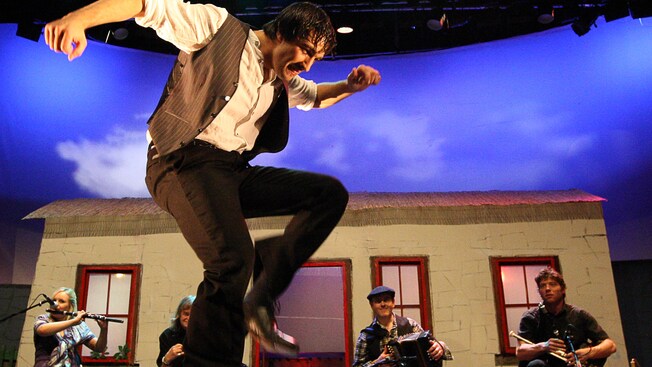 An Irish man doing a jig with his band accompanying him
