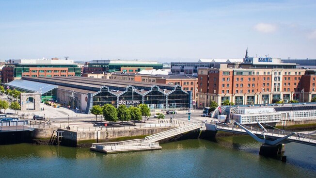 A waterfront with buildings, pedestrians and a bridge