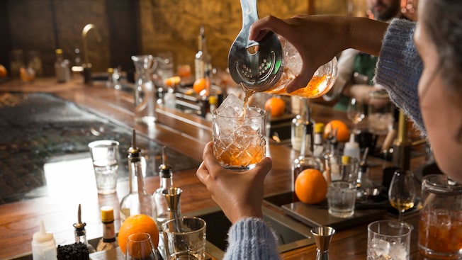 A person pouring whiskey at a bar into a glass with ice A person pouring whiskey at a bar into a glass with ice