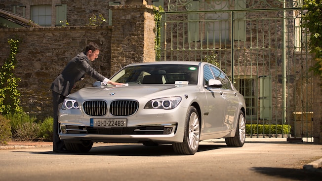 A man in a suit polishes the hood of a sedan A man in a suit polishes the hood of a sedan