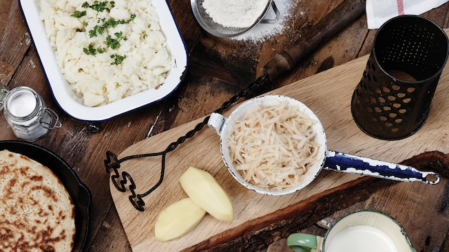 A wood table featuring food in a skillet and a dish, potato shavings, a salt shaker and powder in a sifter A wood table featuring food in a skillet and a dish, potato shavings, a salt shaker and powder in a sifter