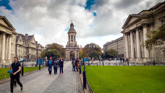 Tourists walking along a cobblestone path on the campus of Trinity College