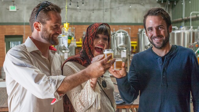 2 men and a woman hold up small glasses of beer in a brewery
