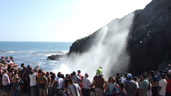 A crowd watches a large spray of water against a rocky cliff A crowd watches a large spray of water against a rocky cliff