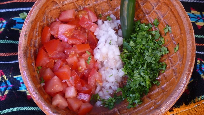 Un chile jalapeño y tomate, cebolla y cilantro picados en un recipiente de terracota