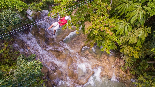A man rides a zip line over a waterfall and a jungle A man rides a zip line over a waterfall and a jungle