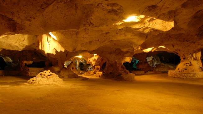 An open cave system with a lights shining from its rocking ceiling and various paths to explore