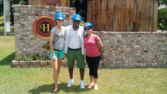 A man flanked by 2 women stands in front of a stone wall at Hampden Estate