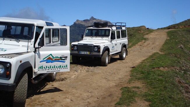 Two jeeps parked on a grassy dirt road