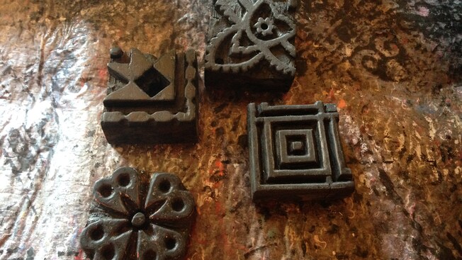 Four square shaped artifacts with geometric and floral designs sit on a table