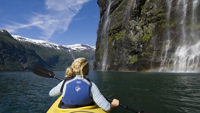 A woman in a kayak looks at waterfalls cascading down a cliffside