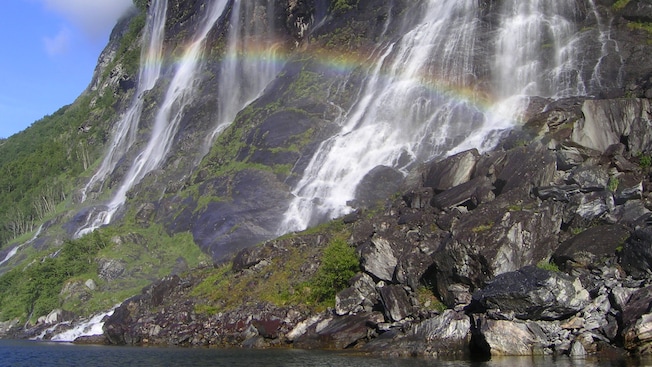 A rainbow and a waterfall near trees and a body of water A rainbow and a waterfall near trees and a body of water