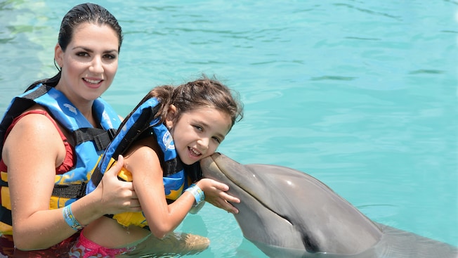 A mother and her young daughter pose with a dolphin in the water
