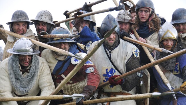 Men, dressed as Scottish warriors from the era of William Wallace, snarl with their spears