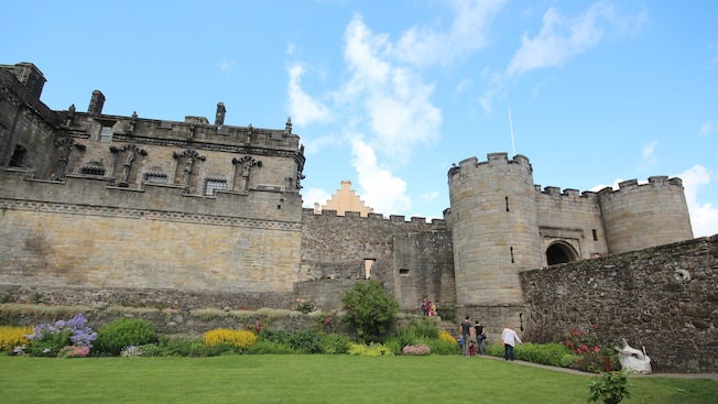 People standing outside Stirling Castle featuring stone walls, flowers and a lawn