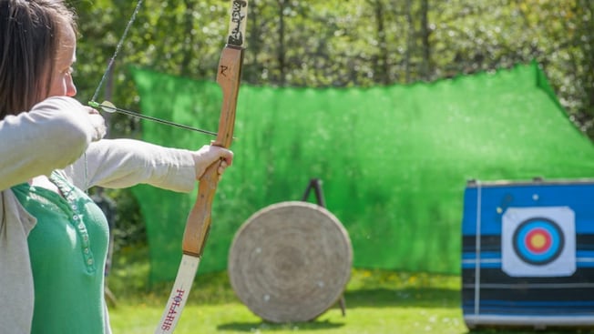 A woman with a bow and arrow aiming for an archery target