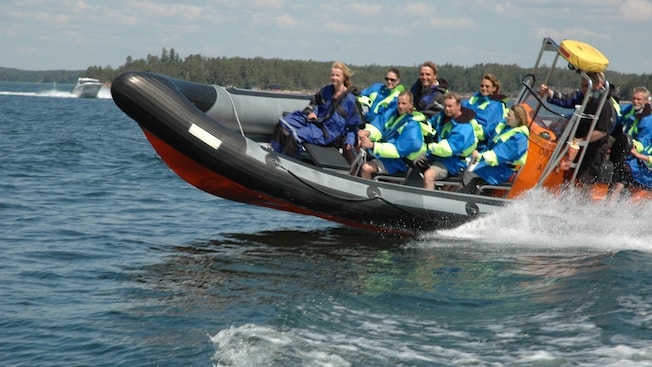Los Visitantes pueden usar chaquetas impermeables mientras viajan en una lancha rápida de goma en el archipiélago finlandés Los Visitantes pueden usar chaquetas impermeables mientras viajan en una lancha rápida de goma en el archipiélago finlandés