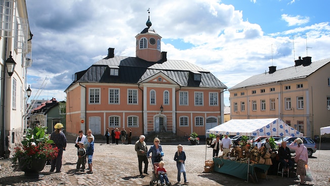 A couple stops to look at flowers for sale outside the Porvoo City Hall while people stroll by