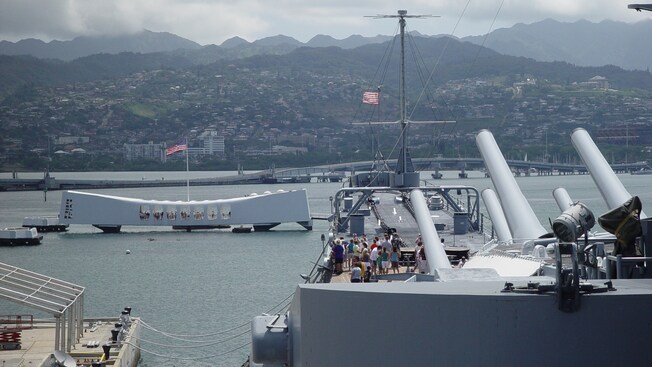 Pasajeros a bordo de la cubierta del USS Missouri miran al otro lado del agua el Monumento conmemorativo del USS Arizona
