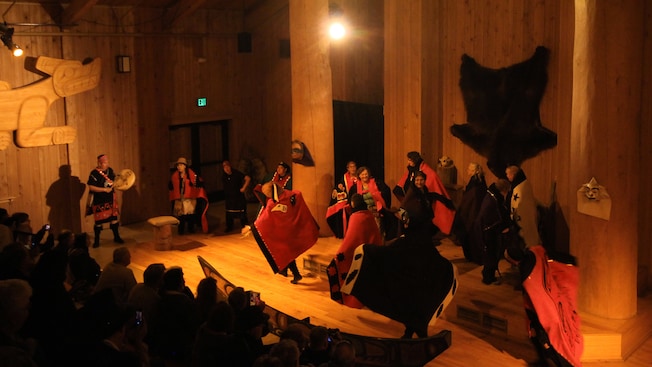 A group of performers dressed in tribal clothing dance and play music before an audience A group of performers dressed in tribal clothing dance and play music before an audience