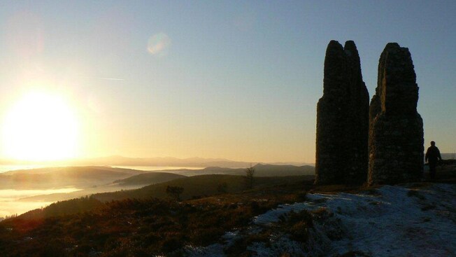 Una puesta de sol ilumina la vista desde un monumento de piedra en una colina