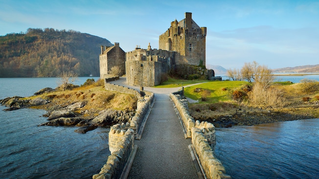 A bridge leads across rippling water to a tiny islet that has an old castle with moss growing on its walls A bridge leads across rippling water to a tiny islet that has an old castle with moss growing on its walls