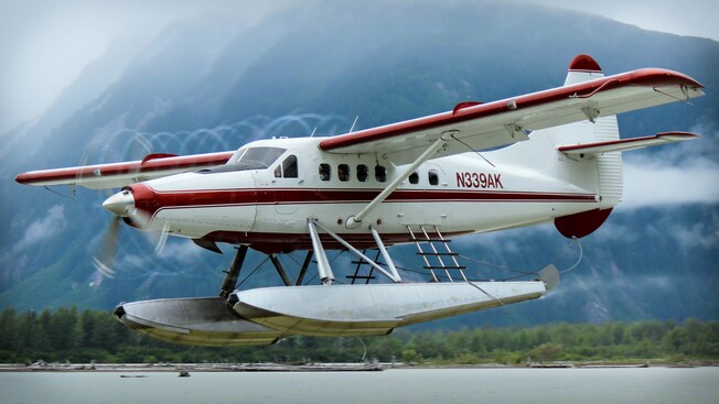 A floatplane lands on a river with a misty mountain in the background