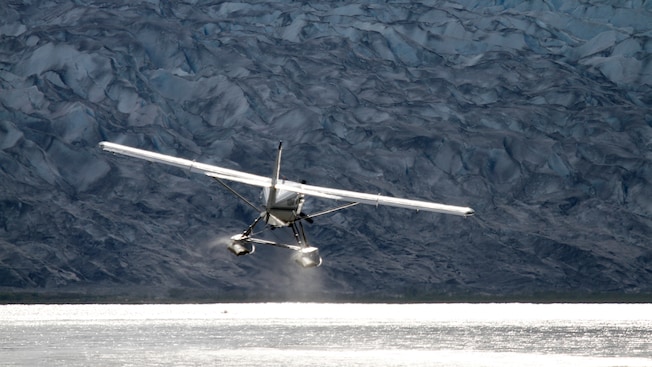 A floatplane approaches the water in front of a huge glacier A floatplane approaches the water in front of a huge glacier