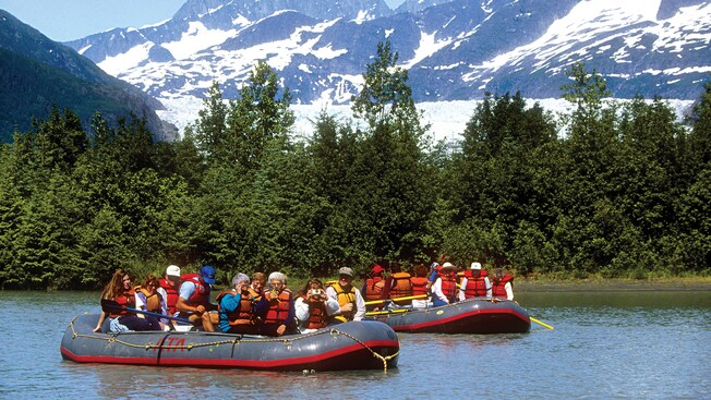 Inflatable rafts filled with people in life jackets float just off the coastline lined with trees