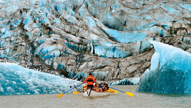 Passengers in a 12 seat canoe paddling up close to a glacier