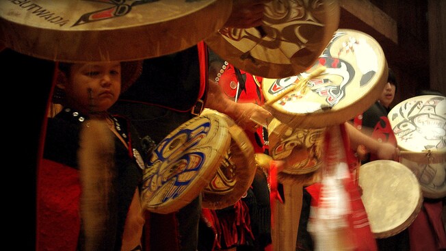 A young boy plays a hand held drum along side a line of drummers in costumes