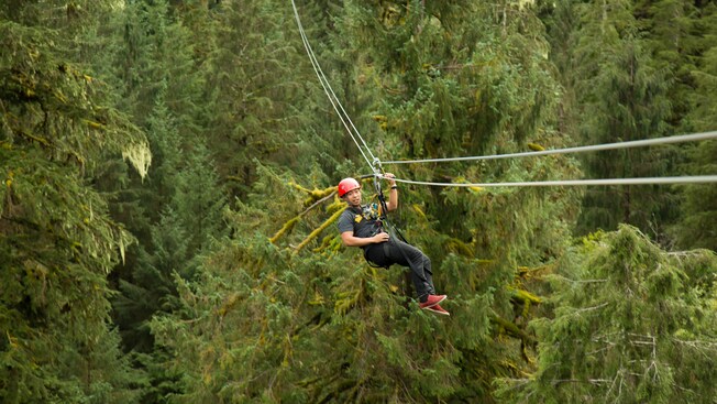 Un hombre con casco colgando de una tirolesa en el bosque
